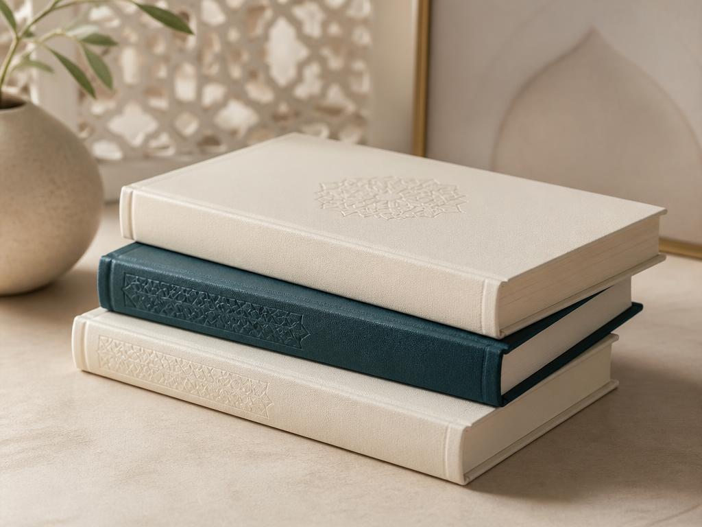 A small stack of elegant cream and teal books with subtle geometric detailing on a neutral surface
